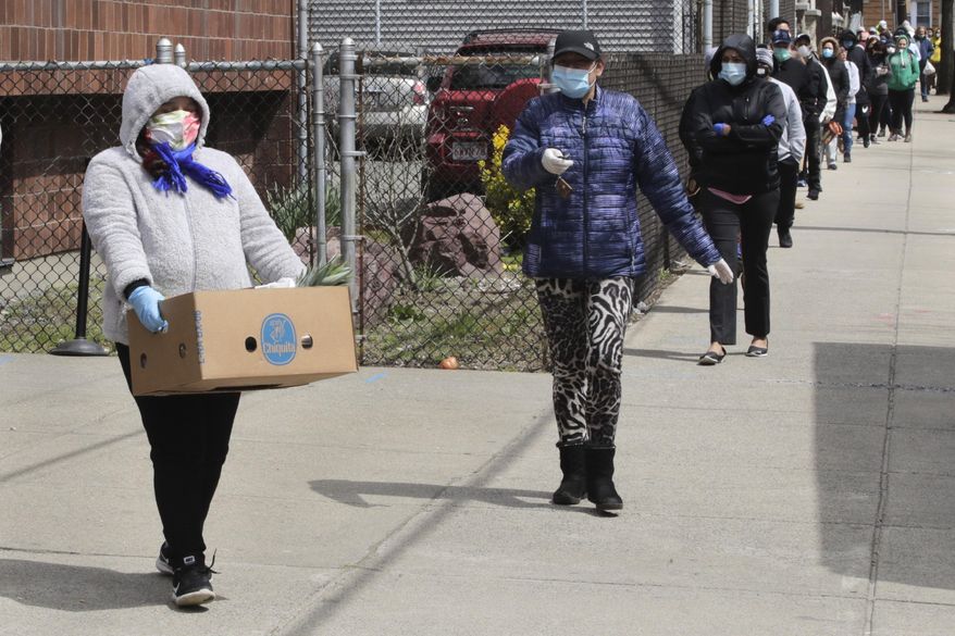A woman carries a box of food away as hundreds others impacted by the COVID-19 virus outbreak wait in line at a Salvation Army center in Chelsea, Mass., Wednesday, April 22, 2020. (AP Photo/Charles Krupa)