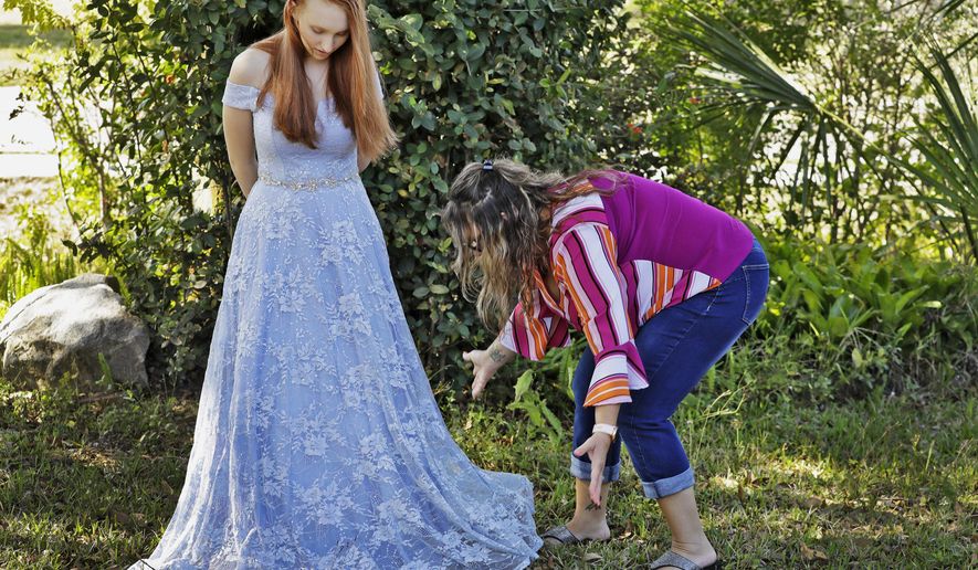 In this April 3, 2020 photo, Annette Reynolds, right, puts the finishing touches on her daughter Amanda's prom gown as she poses for a photo outside their home in Largo, Fla. The Florida teen recently marked her 18th birthday at home, obeying state guidelines and social-distancing rules, by making a cake with her mother and not celebrating with friends as she had planned. Amanda Reynolds is like all of these young people, a case study in what is being lost by those who, in spring 2020, are on the cusp of adulthood and losing many of their expected rites of passage. (AP Photo/Chris O'Meara)