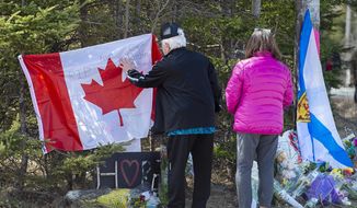 In this Wednesday, April 22, 2020, photo, a couple place a flag at a memorial in Portapique, Nova Scotia, following Saturday&#39;s shooting rampage. (Andrew Vaughan/The Canadian Press via AP)