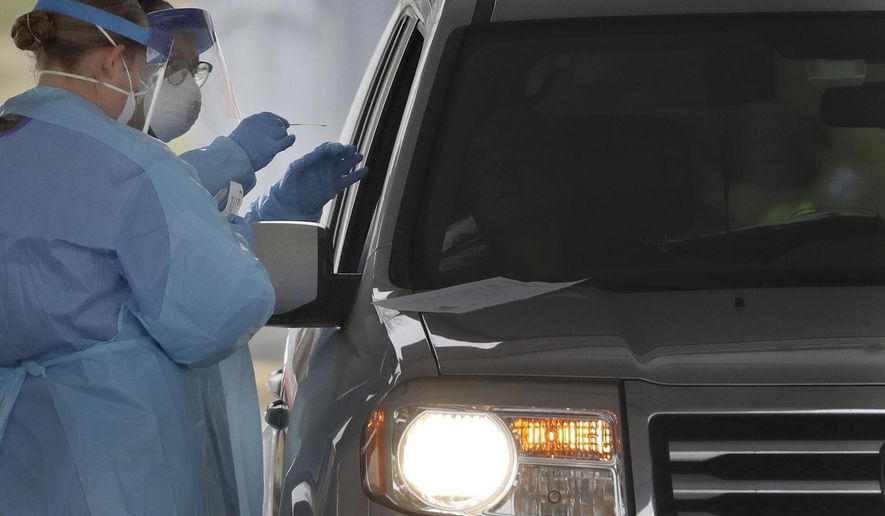 FILE - In this March 20, 2020, file photo, people in protective gear administer a test for the new coronavirus at a drive-thru testing center in Paramus, N.J. Feeling sick and stressed, people in the states hardest hit by the coronavirus have continued to stream into drive-thru testing sites, hoping to get guidance about whether to seek treatment, or reassurance that they aren’t infected. (AP Photo/Seth Wenig, File)
