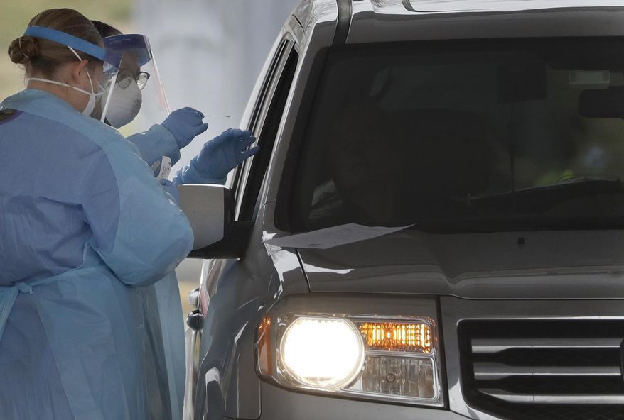 FILE - In this March 20, 2020, file photo, people in protective gear administer a test for the new coronavirus at a drive-thru testing center in Paramus, N.J. Feeling sick and stressed, people in the states hardest hit by the coronavirus have continued to stream into drive-thru testing sites, hoping to get guidance about whether to seek treatment, or reassurance that they aren’t infected. (AP Photo/Seth Wenig, File)