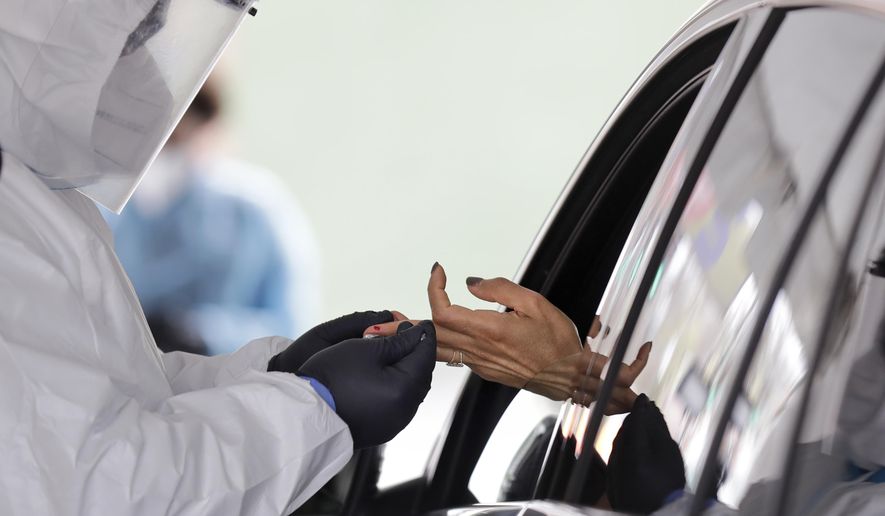 FILE - In this Tuesday, April 14, 2020 file photo, a woman holds her hand out to have blood collected for a 15-minute test for COVID-19 coronavirus antibodies at a drive thru site in Hempstead, N.Y. Antibodies are the markers of infections that someone already had. (AP Photo/Seth Wenig)
