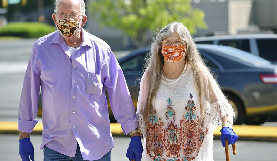 Bud and Elizabeth Neal wear masks to protect agains coronavirus, as they walk through the parking lot after the Anderson Mall opened to limited business on Friday, April 24, 202 in Anderson, S.C. Gov. Henry McMaster eased restrictions on Friday. (AP Photo/Richard Shiro)