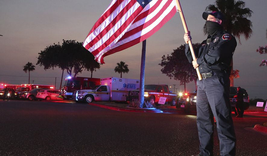 In this Wednesday, April 22, 2020, photo, Edinburg firefighter Homer Garza carries a U.S. flag as Edinburg first responders gather in support of medical staff and their patients at Edinburg Regional Medical Center in Edinburg, Texas. (Joel Martinez/The Monitor via AP)
