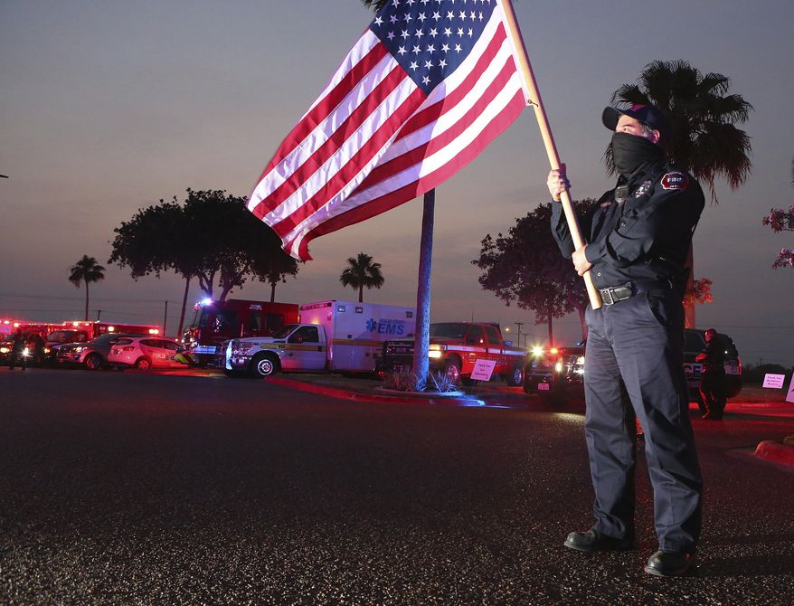 In this Wednesday, April 22, 2020, photo, Edinburg firefighter Homer Garza carries a U.S. flag as Edinburg first responders gather in support of medical staff and their patients at Edinburg Regional Medical Center in Edinburg, Texas. (Joel Martinez/The Monitor via AP)