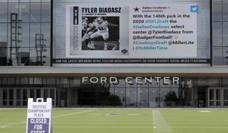 A sign sits on a artificial field frequented by fans at the Ford Center by The Star, the Dallas Cowboys headquarters and training facility, as a large video screen on the exterior wall of the building broadcast the team&#39;s latest selection in the NFL football draft in Frisco, Texas, Saturday April 25, 2020. (AP Photo/Tony Gutierrez)
