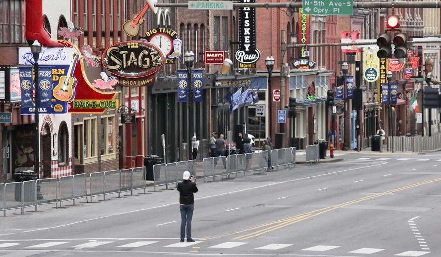 FILE - In this March 23, 2020, file photo, a man stands in the middle of Broadway to take a photo where the streets and sidewalks are normally filled in Nashville, Tenn. Many Nashville musicians have been without steady work for more than five weeks since the city shut down its clubs to slow the spread of the coronavirus. (AP Photo/Mark Humphrey, File)