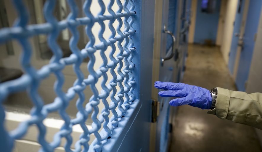 In this April 16, 2020, photo a gloved hand points to a holding cell at the hospital ward of the Twin Towers jail in Los Angeles. Across the country first responders who've fallen ill from COVID-19, recovered have begun the harrowing experience of returning to jobs that put them back on the front lines of America's fight against the novel coronavirus. (AP Photo/Chris Carlson)