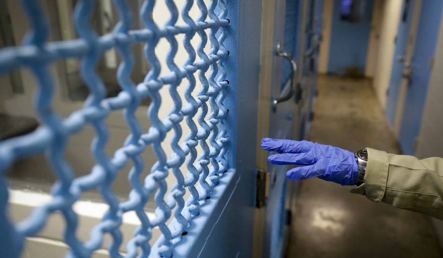 In this April 16, 2020, photo a gloved hand points to a holding cell at the hospital ward of the Twin Towers jail in Los Angeles. Across the country first responders who&#39;ve fallen ill from COVID-19, recovered have begun the harrowing experience of returning to jobs that put them back on the front lines of America&#39;s fight against the novel coronavirus. (AP Photo/Chris Carlson)