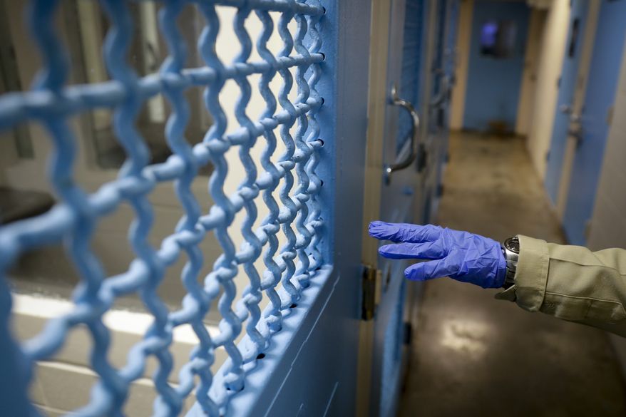 In this April 16, 2020, photo a gloved hand points to a holding cell at the hospital ward of the Twin Towers jail  in Los Angeles. Across the country first responders who&#x27;ve fallen ill from COVID-19, recovered have begun the harrowing experience of returning to jobs that put them back on the front lines of America&#x27;s fight against the novel coronavirus. (AP Photo/Chris Carlson)