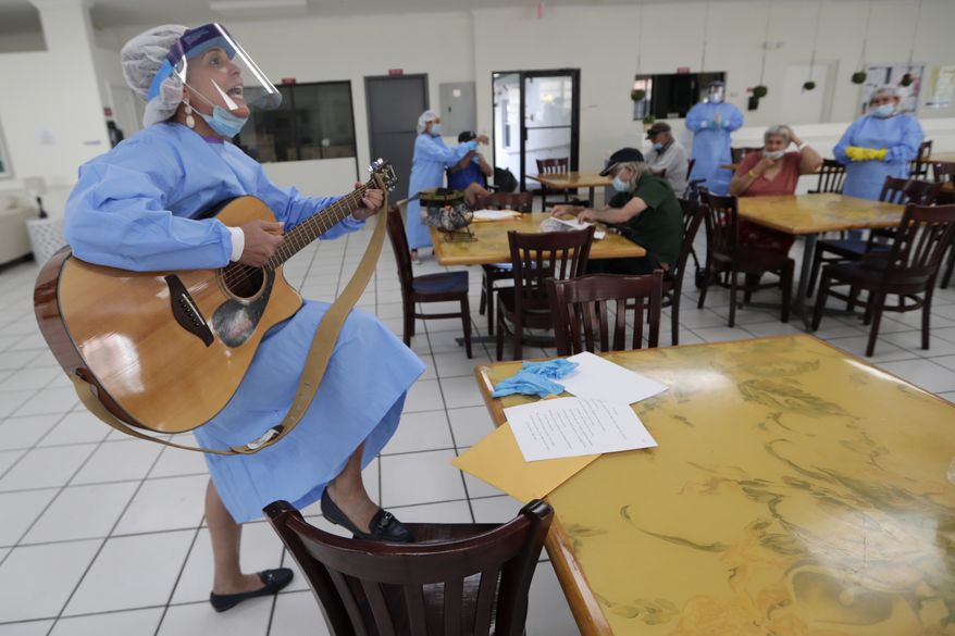 Roxana Solano wears personal protective equipment as she plays the guitar and sings as residents sing along at a temporary quarantine and isolation facility for the homeless during the new coronavirus pandemic, Monday, April 27, 2020, in North Miami, Fla. This location houses people 60 and older who were living in shelters, on the street or were known to have health issues making them vulnerable to COVID-19. (AP Photo/Lynne Sladky ** FILE **)