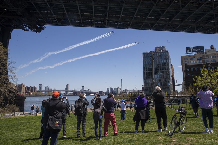Spectators watch from the Brooklyn bridge park as a formation of U.S. Navy Blue Angels and U.S. Air Force Thunderbirds fly over the East River, Tuesday, April 28, 2020, in New York. The flyover was in salute to first responders in the fight against the new coronavirus. (AP Photo/Mary Altaffer)