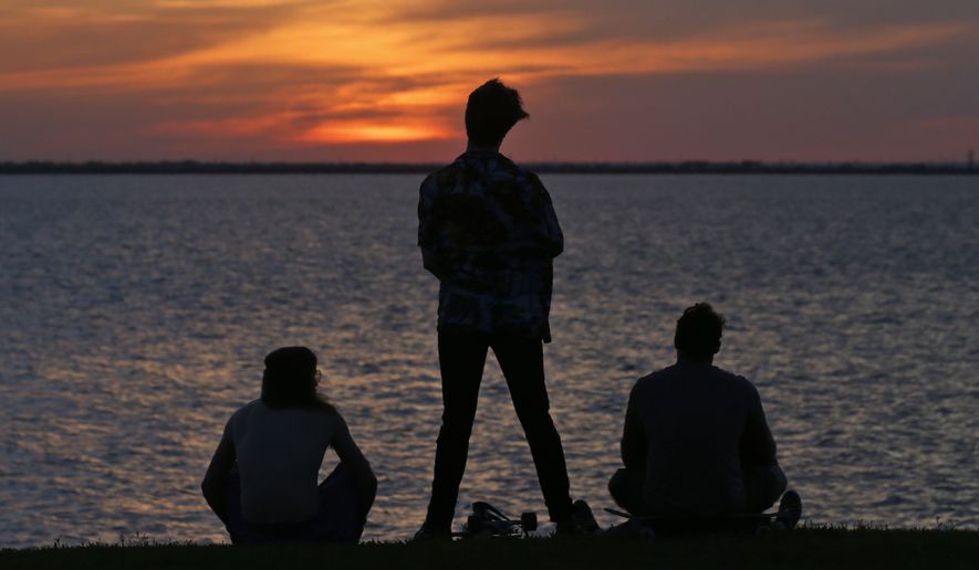People watch from shore as the sun sets at Lake Hefner, Monday, April 27, 2020, in Oklahoma City.  (AP Photo/Sue Ogrocki)