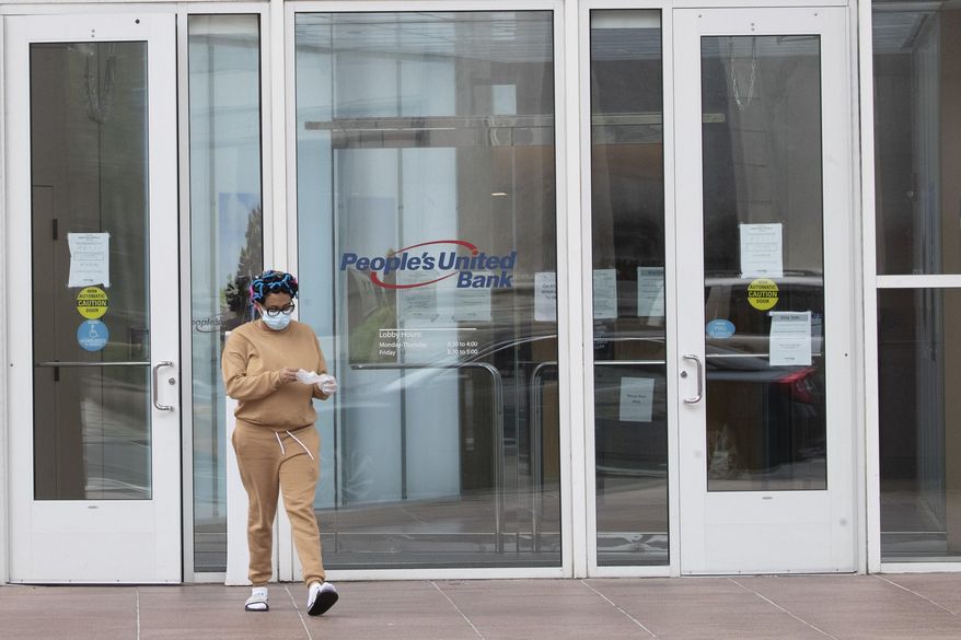 A woman wearing a face mask to protect against the coronavirus takes off disposable gloves after using an ATM at the People's United Bank on Main Street in downtown in Bridgeport, Conn, Monday, April 27, 2020. (AP Photo/Mary Altaffer)