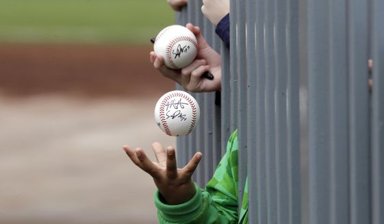 In this March 10, 2020, file photo, a child tosses an already-autographed baseball while awaiting another signature from a passing player before a spring training baseball game between the Los Angeles Angels and the Seattle Mariners in Peoria, Ariz. Doctors, scientists and sports leaders are outlining the path back to playing fields for children in grassroots sports -- an exercise that could inform major organizations on how to get their industries up and running as well in the midst of the COVID-19 pandemic. (AP Photo/Elaine Thompson, File) **FILE**