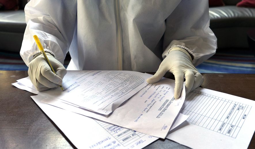 In this April 24, 2020, photo, a doctor fills a form for the second swab test of Associated Press photographer Rafiq Maqbool at a hotel room where the photographer is in quarantine, in Mumbai, India. Maqbool was tested positive for COVID-19 with dozens of other journalists, who were then moved collectively to a hotel turned quarantine center. He left his wife and children home alone to deal with a sealed building, anxious relatives and the stigma of being related to someone who had caught the virus. On the seventh day, the test from his second swab test turned out negative and he was allowed to return home to be under home quarantine for 14 days. (AP Photo/Rafiq Maqbool)