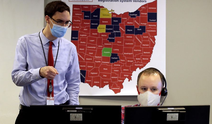 Ohio election official Brian Katz, right, and Dave Ward look over the early returns in the Ohio primary election in the election night reporting center in Columbus, Ohio, while wearing masks during the coronavirus pandemic Tuesday, April 28, 2020. (AP Photo/Gene J. Puskar)