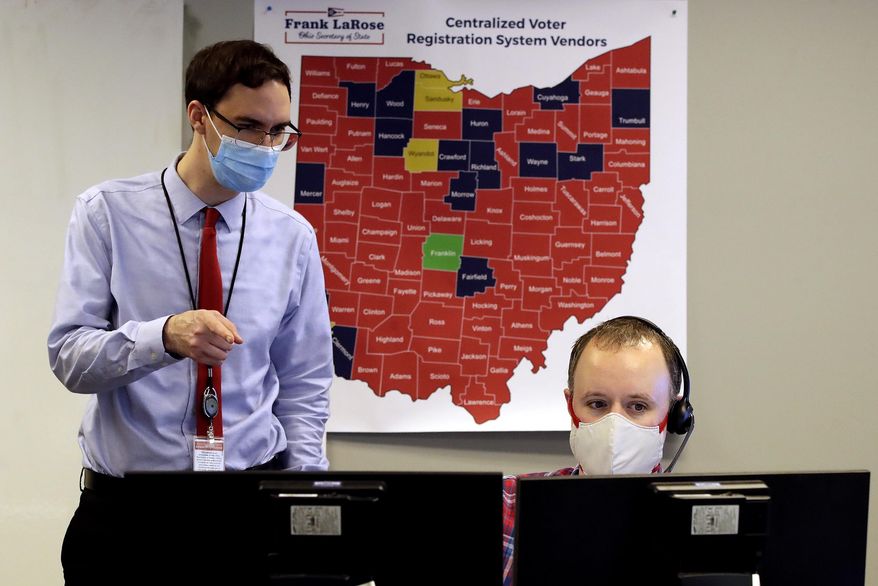 Ohio election official Brian Katz, right, and Dave Ward look over the early returns in the Ohio primary election in the election night reporting center in Columbus, Ohio, while wearing masks during the coronavirus pandemic Tuesday, April 28, 2020. (AP Photo/Gene J. Puskar)