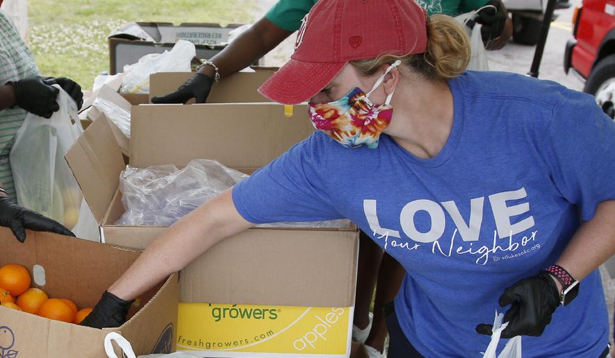 Candice Hillenbrand, of St. Luke's United Methodist Church and Ending Hunger OKC, reaches for an orange to add to a produce bag at a food give-away at Christ Temple Community Church, Tuesday, April 28, 2020, in Oklahoma City, as the need for food assistance grows during the coronavirus pandemic. (AP Photo/Sue Ogrocki)