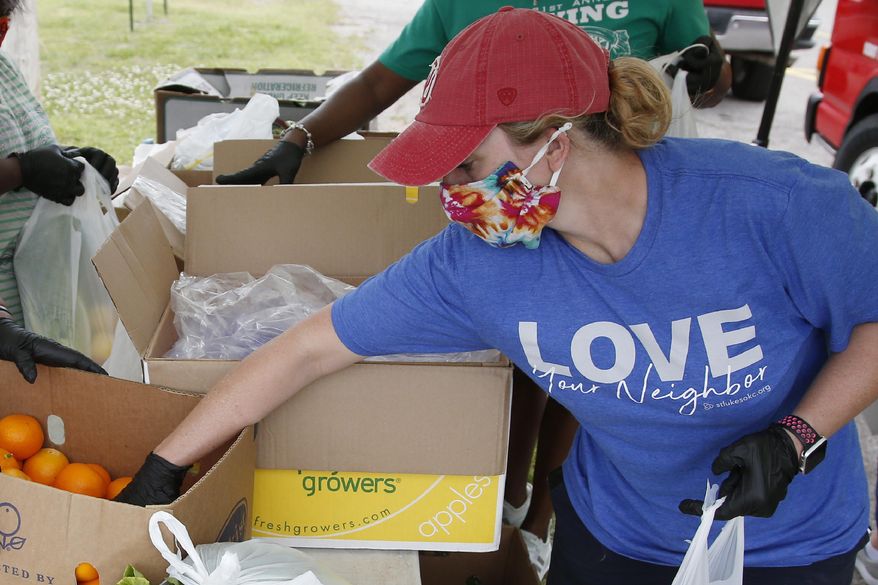 Candice Hillenbrand, of St. Luke's United Methodist Church and Ending Hunger OKC, reaches for an orange to add to a produce bag at a food give-away at Christ Temple Community Church, Tuesday, April 28, 2020, in Oklahoma City, as the need for food assistance grows during the coronavirus pandemic. (AP Photo/Sue Ogrocki)
