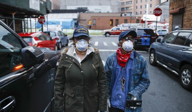Sandra Perez, left, and Fransisco Ramirez, right, stand outside Elmhurst Hospital Center after delivering a box of donated groceries to a man in need, Saturday, April 18, 2020, in the Queens borough of New York. Some are former construction workers or cleaning ladies who lost their jobs and can barely pay rent, but they go out each day to deliver donated diapers, formula or food to families in need. Through Spanish-speaking chats in Facebook or word of mouth, small groups of immigrants find out who needs the help and they deliver it traveling by car or by foot, exposing themselves to the coronavirus that has already hit hard working-class neighborhoods. (AP Photo/John Minchillo)
