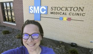 In this Wednesday, April 29, 2020 photo selfie provided by Dr. Beth Oller, Oller, a family physician, smiles while standing outside her medical clinic, just south of Main Street in Stockton, Kan. Oller began preaching social distancing well before her home of Rooks County confirmed its first coronavirus case and now she&#39;s nervous about the state reopening its economy too soon. (Dr. Beth Oller via AP)