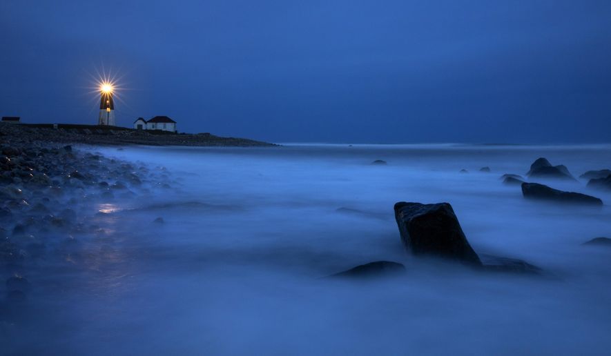 Waves wash over rocks as a beacon of light shines across the rocky shore from the Point Judith Lighthouse in Narragansett, R.I., Saturday, April 25, 2020. (AP Photo/David Goldman)