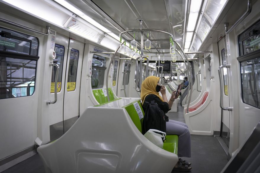A woman wearing a protective mask uses her phone in a Light Rail Transit train, during the movement control order due to the outbreak of the coronavirus disease COVID-19 in Kuala Lumpur, Malaysia, on Friday, May 1, 2020. Malaysia will allow most business activities to reopen from May 4, Malaysian Prime Minister Muhyiddin Yassin says the economy needs to be revived as billions have been lost during the partial lockdown that began in March. (AP Photo/Vincent Thian)