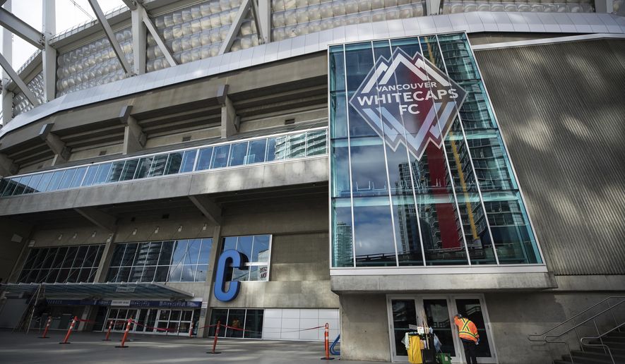 A worker cleans a door handle at B.C. Place stadium, where Major League Soccer's Vancouver Whitecaps play their home games, in Vancouver, British Columbia, Thursday, March 12, 2020. Major League Soccer is shutting down for 30 days because of the coronavirus, the league announced Thursday. (Darryl Dyck/The Canadian Press via AP)