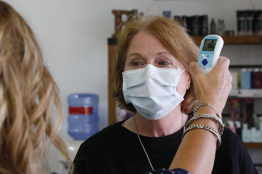 Denise Gavitt, left, takes the temperature of incoming client Brenda Hornbeek, right, as Hornbeek arrives for her appointment at Gavitt's salon, Beehive Salon, Friday, May 1, 2020, in Edmond, Okla., the first day hair salons have been allowed to reopen in Edmond following shutdowns due to coronavirus concerns. (AP Photo/Sue Ogrocki)