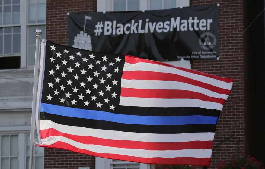 FILE - In this July 28, 2016, file photo, a flag with a blue and black stripes in support of law enforcement officers, flies at a protest by police and their supporters outside Somerville City Hall in Somerville, Mass. San Francisco's police chief said the city's rank and file will wear neutral face coverings to defuse a controversy that was sparked when officers sent to patrol a May Day protest wore masks adorned with the "thin blue line" flag. (AP Photo/Charles Krupa, File)