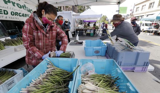 Farmer Alegria Canales stacks asparagus as a customer behind completes his purchase at her family&#x27;s stand in the West Seattle Farmers Market during its first opening in nearly two months because of the coronavirus outbreak Sunday, May 3, 2020, in Seattle. (AP Photo/Elaine Thompson)  **FILE**