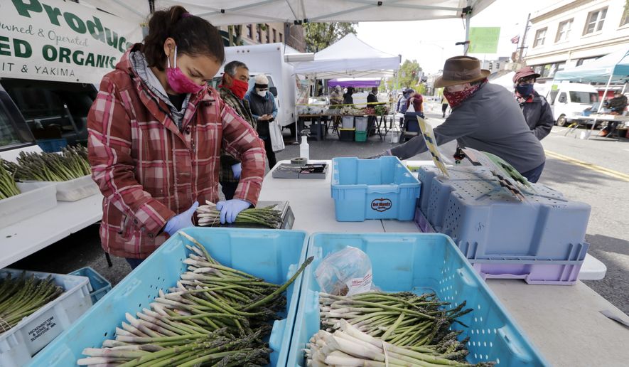 Farmer Alegria Canales stacks asparagus as a customer behind completes his purchase at her family's stand in the West Seattle Farmers Market during its first opening in nearly two months because of the coronavirus outbreak Sunday, May 3, 2020, in Seattle. (AP Photo/Elaine Thompson) **FILE**