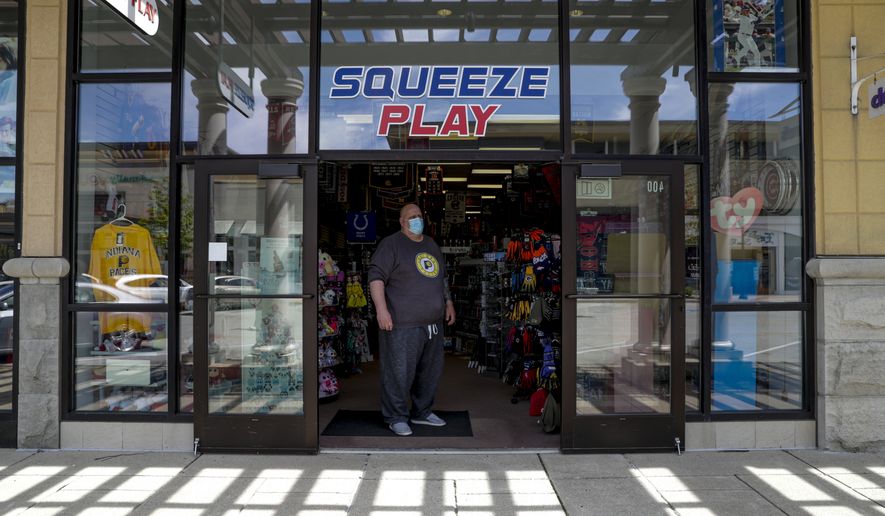 Tony Myers waits for customers in the doorway to Squeeze Play a team sports memorabilia and clothing store in the Hamilton Town Center in Noblesville, Ind., Monday, May 4, 2020. Indiana allowed real stores to open with capacity after restrictions put in place to curb the spread of the new coronavirus were rolled back. Less than 20 percent of the stores in the shopping center were open. (AP Photo/Michael Conroy)