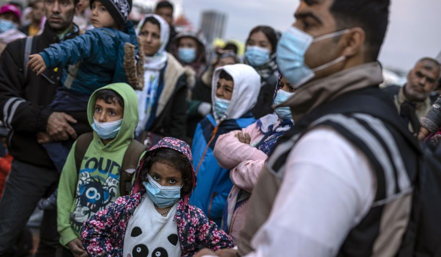 Refugees and migrants wearing masks to prevent the spread of the coronavirus, wait to get on a bus after their arrival at the port of Piraeus, near Athens on Monday, May 4, 2020. Greek authorities are moving 400 migrants, mostly families, to the mainland to help ease overcrowded conditions at the camp Moria in Lesbos island. (AP Photo/Petros Giannakouris)