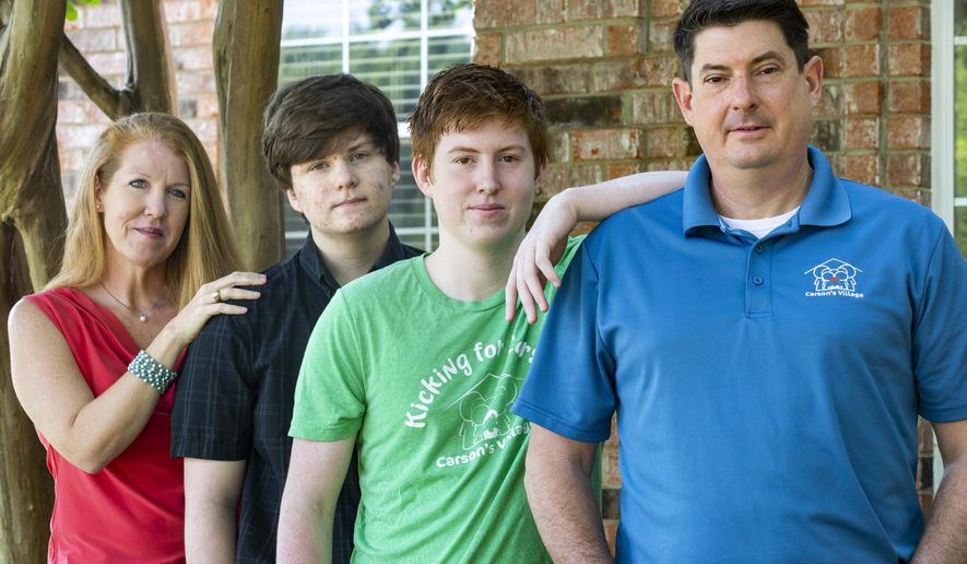 Jason Dyke, right, and his wife, April, left, pose for a portrait with their sons Ryan and Alex at their home in Coppell, Texas, Tuesday, April 21, 2020. Another son, Carson, died by suicide at age 11 three years ago, and the parents have since created Carson's Village — a nonprofit aiming to help families navigate the grief and loss of loved ones with resources and advice. The coronavirus pandemic has complicated that work, but it has also led to new ways to help families of COVID-19 victims or those who have died from other causes during this difficult time. (Lynda M. Gonzalez/The Dallas Morning News via AP)