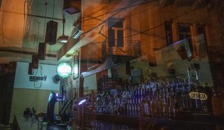 In this Sunday, May 3, 2020, photo, balconies of an old building are reflected in the glass door of a closed bar during the coronavirus pandemic, in central Beirut, Lebanon. The owners of some of Lebanon’s best-known clubs have pulled together a three-day non-stop virtual music festival. This time, 150 DJs from around the world are playing for a cause. They&#39;re collecting donations for the thousands of servers, bartenders, waiters and other daily wage earners who have been without a job since coronavirus restrictions forced a shutdown in mid-March. (AP Photo/Hassan Ammar)