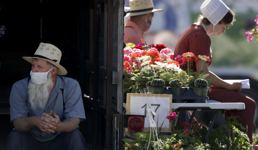 Vendors wait for customers at a drive-thru farmers market Saturday, May 2, 2020, in Overland Park, Kan. The market has moved from its usual home to a sprawling parking lot allowing for people to spread out and shop from their cars as a measure to stem the spread of COVID-19. (AP Photo/Charlie Riedel)