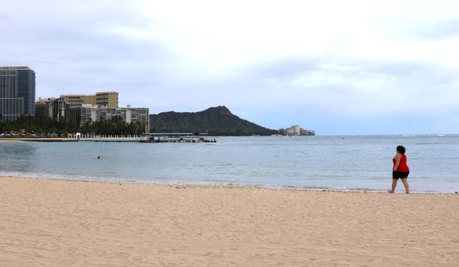 In this April 21, 2020, photo, a woman walks on Waikiki Beach in Honolulu. Hawaii has some of the lowest coronavirus infection and mortality rates in the U.S. (AP Photo/Caleb Jones)  **FILE**