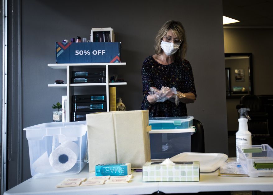 Marti Brown, an owner and operator of the Town and Country Barber Shop and Salon located at 125 North Market Street, puts on protective gloves as she sorts through sanitary items on Tuesday, May 5, 2020 in Chattanooga, Tenn. Barber shops and salons across Tennessee will be reopening Wednesday, with strict regulations in order to maintain social distancing practices put in place to stop the spread of coronavirus. (Troy Stolt/Chattanooga Times Free Press via AP)