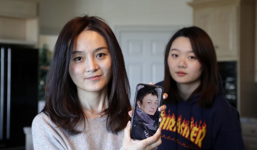 Jodie Chen, left, holds a photo of her husband, Daniel Hsu, as their daughter, Mandy Luo, looks on in their home in Issaquah, Wash., on Monday, April 13, 2020. The family is waiting for husband and father Daniel Hsu to be allowed to leave China and return home. (AP Photo/Elaine Thompson)