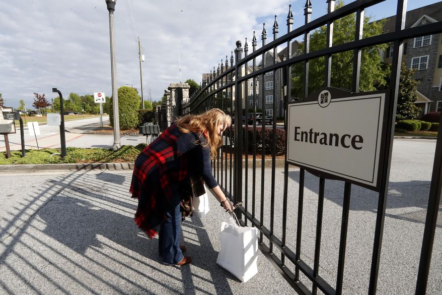 Crystal Craft places a bag of food at the gate for her husband, Justin, before sitting down for their weekly dinner date on opposite sides of a fence surrounding the Park Springs senior community, where Justin runs the food and beverage department, Thursday, April 30, 2020, in Stone Mountain, Ga. Since the end of March, Park Springs has had employees live on its 61-acre campus instead of commuting from home _ an unusual approach, even as nursing homes have been among the hardest-hit places by the coronavirus. (AP Photo/John Bazemore)