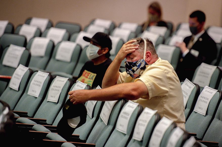 A man wearing a protective face mask rests his head in his hand while sitting during the Riverside County Board of Supervisors meeting to decide whether to lift coronavirus health orders in Riverside, Tuesday, May 5, 2020. (Watchara Phomicinda/The Orange County Register via AP)
