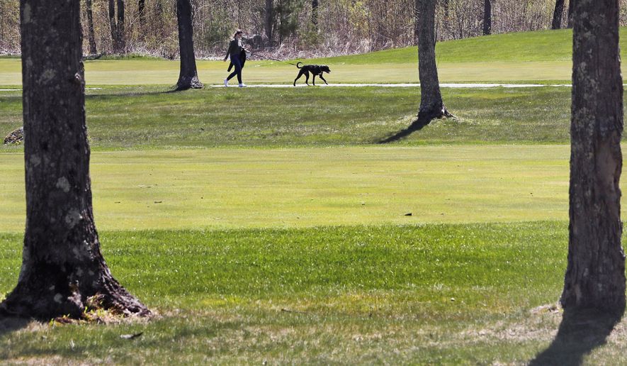 A woman walks a dog on a cart path of a golf course, which was closed along with many other nonessential businesses due to the COVID-19 virus outbreak, at the Atkinson Country Club in Atkinson, N.H., Tuesday, May 5, 2020. Golf courses across the state are expected to reopen for New Hampshire residents and members on May 11, as some virus lockdown measures are lifted. (AP Photo/Charles Krupa)