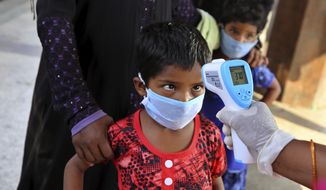 An Indian health worker checks the temperature of a child who had been stranded for weeks due to the lockdown to curb the spread of new coronavirus before allowing her to board a bus, in Bangalore, India, Wednesday, May 6, 2020. India partly relaxed its lockdown this week. (AP Photo/Aijaz Rahi)