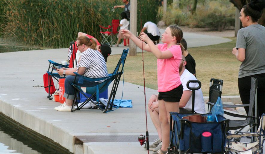 In this April 30, 2020 photo, a girl checks her line as people fish at Veterans Oasis Park in Chandler, Ariz. Many state fishing programs have continued to stock community lakes during the coronavirus pandemic, allowing people who have been locked up for weeks a chance to enjoy the outdoors. (AP Photo/John Marshall)