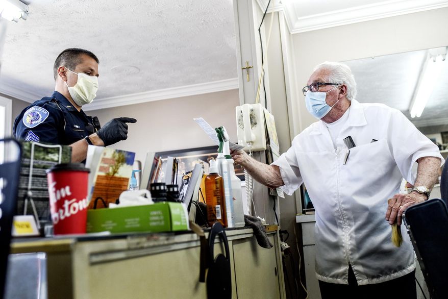 An Owosso police officer asks to talk with Karl Manke outside before ticketing Karl for being open at Karl's barber shop on Wednesday, May 6, 2020, at in Owosso, Mich. Salons and barber shops have been closed by Gov. Gretchen Whitmer, who said they're not essential during the coronavirus outbreak.(Nick King/Lansing State Journal via AP)