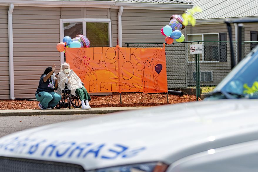 In this Wednesday, May 6, 2020 photo, Ruth Evelyn Harrington, right, and certified nursing assistant Stacie Coleman wave during a birthday party for Harrington at River's Bend Retirement Community, in Kuttawa, Ky. The parade marked Harrington's 109th birthday, which could not be held in person due to restrictions in the midst of the COVID-19 pandemic. (Dave Thompson/The Paducah Sun via AP)