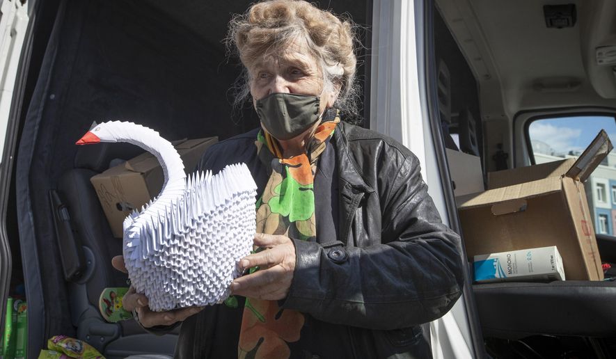 In this photo taken on Thursday, April 30, 2020, Galina Yakovleva holds an origami swan made by her, near her van in St.Petersburg, Russia. Every day amid the coronavirus pandemic, 80-year-old Leningrad siege survivor Galina Yakovleva has driven to the city in her white minivan to bring charity groceries and goods to elderly people and families with children in need. (AP Photo/Dmitri Lovetsky)