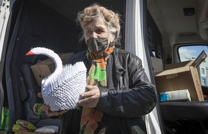 In this photo taken on Thursday, April 30, 2020, Galina Yakovleva holds an origami swan made by her, near her van in St.Petersburg, Russia. Every day amid the coronavirus pandemic, 80-year-old Leningrad siege survivor Galina Yakovleva has driven to the city in her white minivan to bring charity groceries and goods to elderly people and families with children in need. (AP Photo/Dmitri Lovetsky)